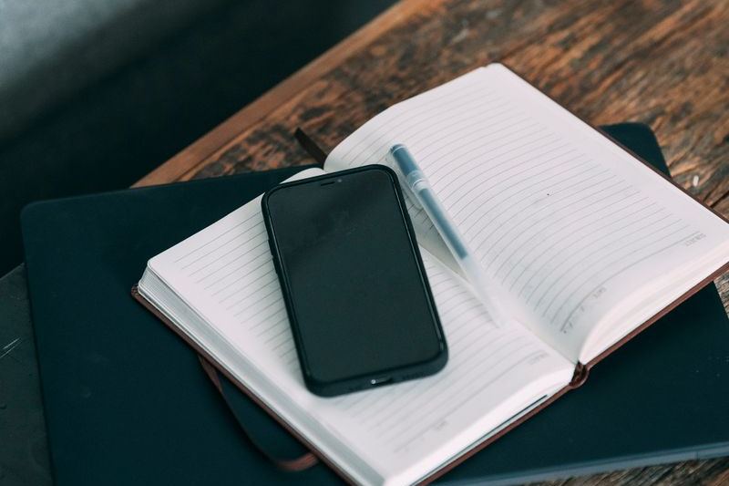 An open notebook with a pen and a phone on a wooden desk