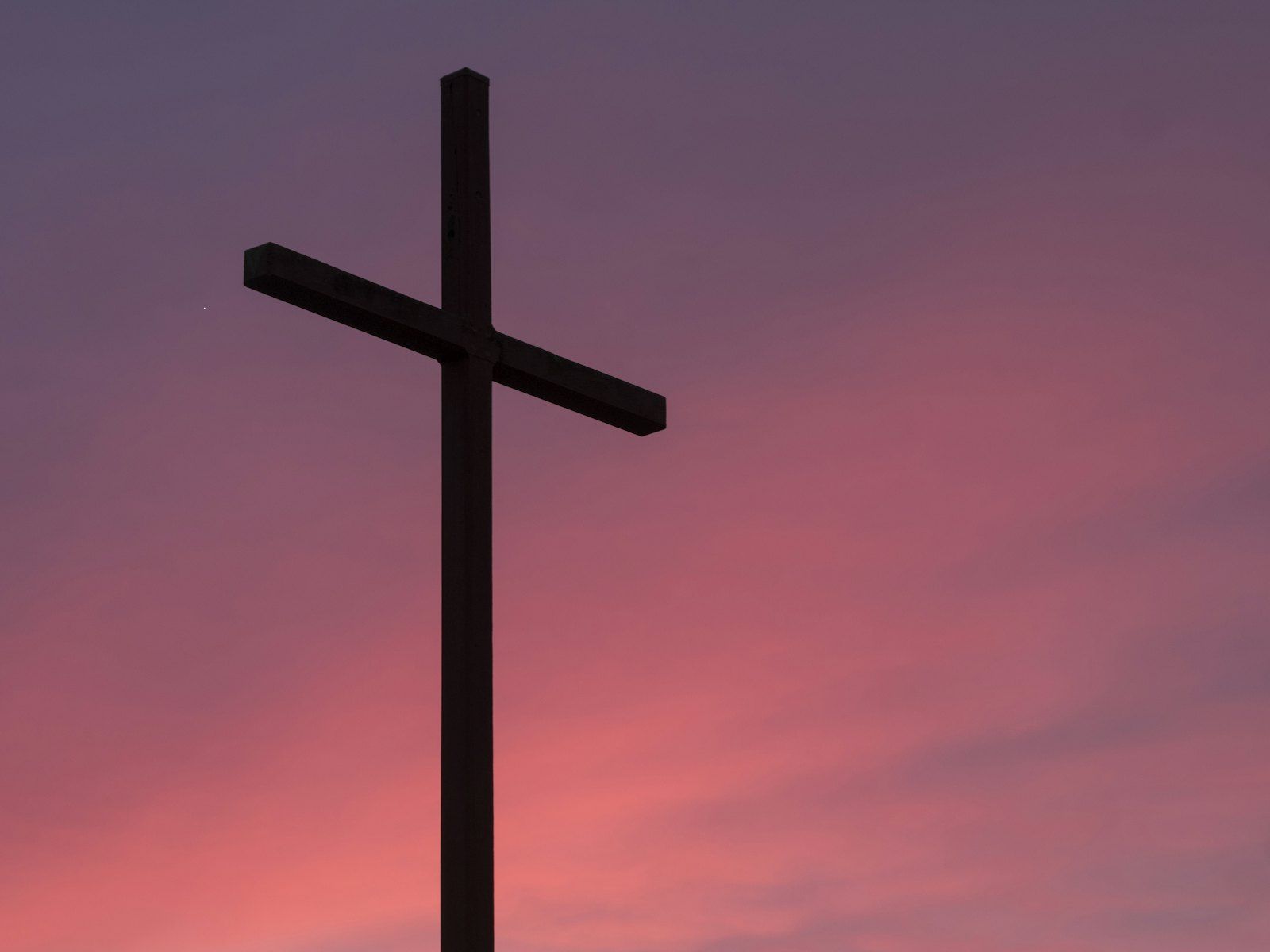 A simple wooden cross silhouetted against a pink and purple evening sky